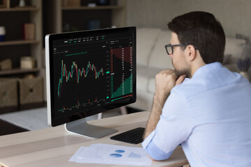 Serious man trader, analyst make stock market research, looks at pc screen learn information in charts and graphs, screen view with digital data over male shoulder. Crypto-currency, trading, analytics