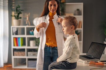 Female doctor checking child during medical checkup at home interior