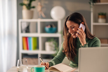 Businesswoman working at home while talking on a phone and taking notes