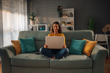 Smiling caucasian woman using laptop while sitting on couch at home