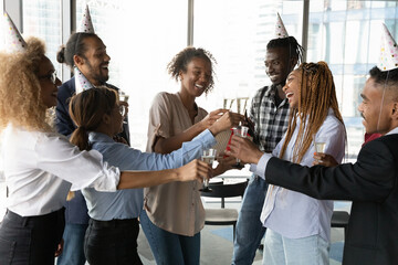 Raising glasses to success. Overjoyed diverse biracial colleagues have fun celebrate reward for...
