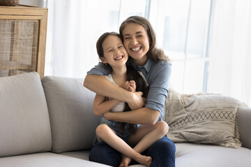 Loving mother sit on sofa cuddling tightly her little daughter, feeling pure love to child, spend...