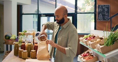 Young man pouring pasta into bag, buying healthy goods from reusable containers with organic bulk...
