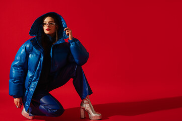 Fashionable confident woman wearing trendy oversized blue puffer jacket, sunglasses, leather pants,...