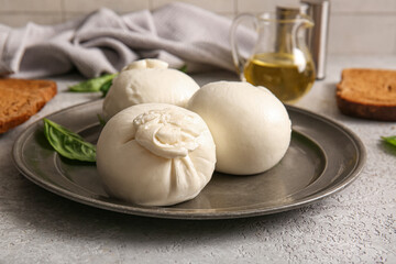 Plate of tasty Burrata cheese with basil on grey table