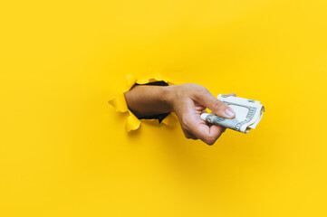 A female hand appears in the hole in torn yellow paper and squeezes two hundred-dollar bills....