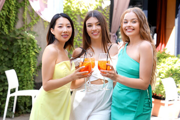 Beautiful young women with glasses of tasty aperol spritz cocktail spending time in cafe, outdoors