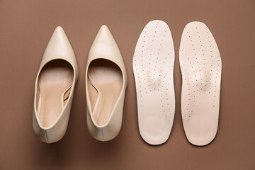 Pair of orthopedic insoles and high heeled shoes on color background