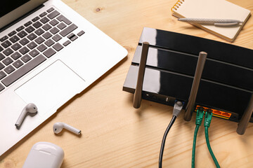 Modern wi-fi router with laptop and earphones on wooden background