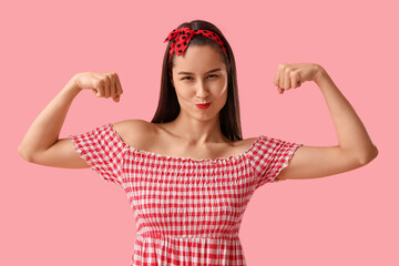 Portrait of strong pin-up woman showing muscles on pink background. Women's History Month