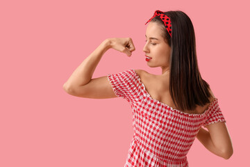 Portrait of strong pin-up woman showing muscles on pink background. Women's History Month