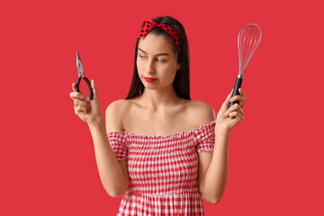 Portrait of young pin-up woman with whisk and pliers on red background. Women's History Month