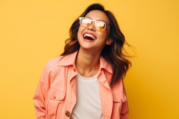 Portrait of a happy young woman in sunglasses over yellow background.