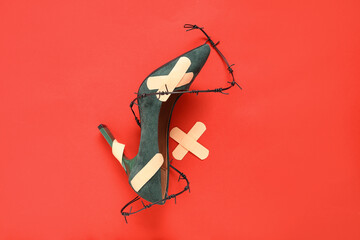 High-heeled shoe with plasters and barbed wire on red background. Uncomfortable shoes concept