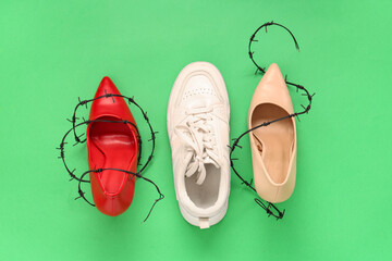 Sneaker and high-heeled shoes wrapped in barbed wire on green background. Uncomfortable shoes concept