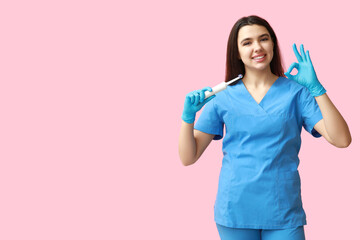 Female dentist with electric toothbrush showing ok gesture on pink background. World Dentist Day