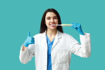 Female dentist with electric toothbrush showing thumb-up gesture on blue background. World Dentist Day