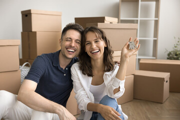 Cheerful excited young couple happy to move into new house, showing keys, hugging at stacked...