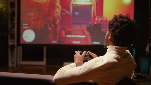 Close up of man playing shooter videogame, searching for loot in dark industrial halls. Gamer participating in PvP online multiplayer game using console attached to ultrawide smart TV, zoom in