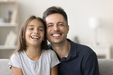 Obraz na płótnie Canvas Cheerful handsome dad and carefree cute girl kid looking at camera with toothy smile, promoting family dental care, healthy white teeth. Happy father and pretty daughter home head shot portrait