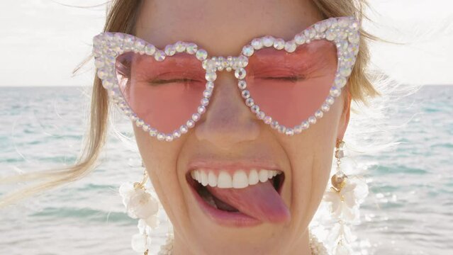 Portrait smiley woman in pink glasses fools around and shows tongue. Positive girl having good time, blowing air kiss. Surprised lady with wide-opened eyes. Close up happy emotional bride on honeymoon