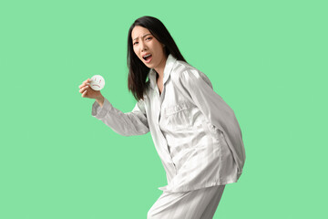 Young Asian woman in pajamas with hemorrhoids and sad smile on green background