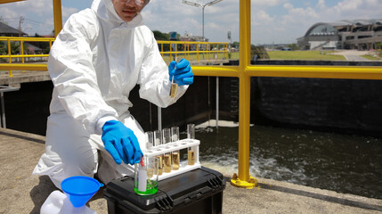 Water analysis operator wearing PPE examining  and auditing water from the water treatment plant,...