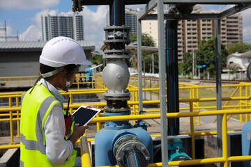 a female engineer is wearing a protective helmet on her head, using tablet Analytics engineering data. at the wastewater treatment plant