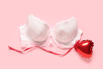 White female bra and heart-shaped balloon on pink background. Valentine's Day celebration