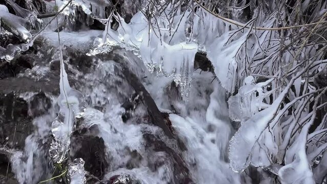 The clear water of a mountain stream in the European Alps has frozen in the morning frost into artistic icicles, the fast flow is murmuring musically