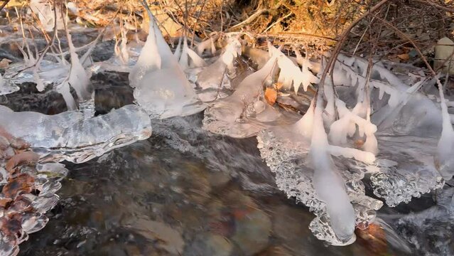 The clear water of a mountain stream in the European Alps has frozen in the morning frost into artistic icicles, the fast flow is murmuring musically
