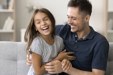 Cheerful loving daddy tickling excited shouting daughter kid, laughing, having fun at home with child, enjoying fatherhood, playtime. Happy girl playing active games with dad - obrazy, fototapety, plakaty