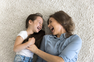 Top above view of cheerful little girl enjoy playtime with mother, lying together on carpet enjoy...