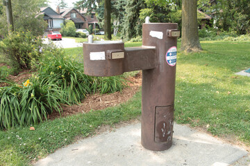 brown public double water drinking fountain with second leveraged out on cement slab in park...