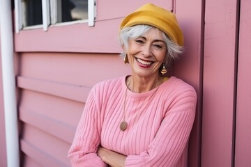 Portrait of happy senior woman with yellow hat standing by pink wall