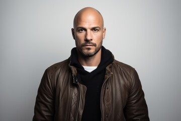 Portrait of a bald man in a leather jacket on a gray background.