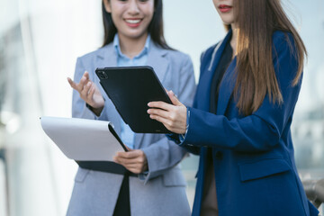 Portrait of two stylish pretty women standing and holding laptop and mobile phones.