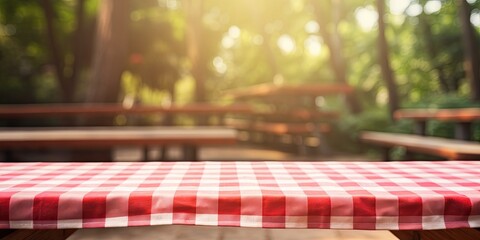 Picnic table with a red checkered towel, empty space, and a blurred wooden deck backdrop. Promotion display.