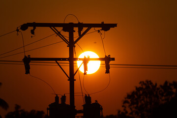 Silhouette of high voltage electric pole with sun at sunset.