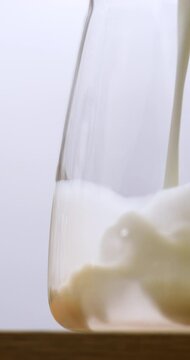 4K footage vertical video Front view SLO MO CU, Pouring fresh milk into a clear glass pitcher on a white background.