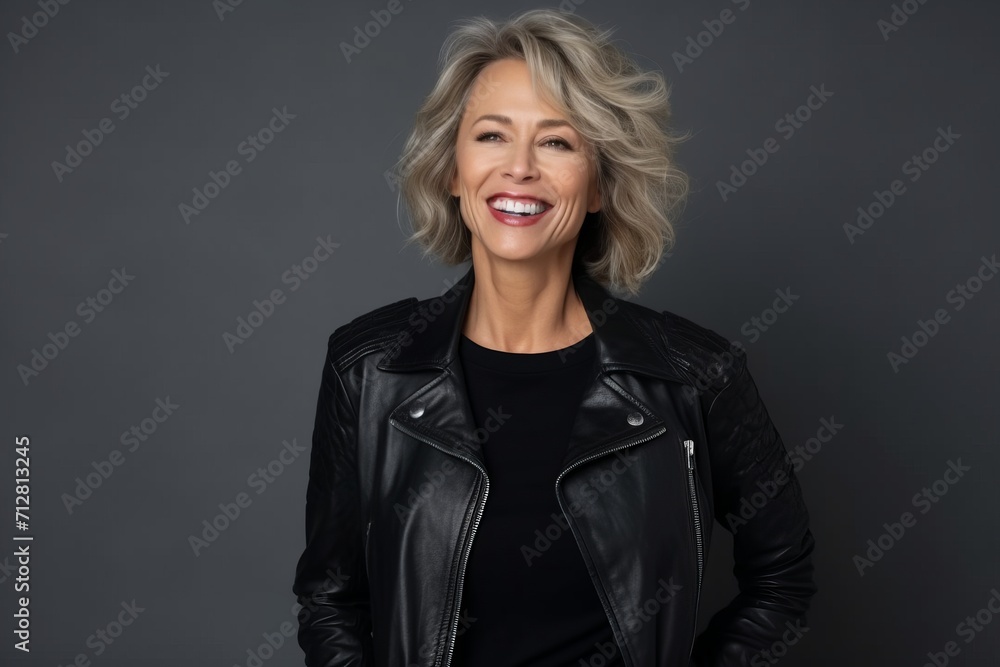 Poster Portrait of a happy senior woman in leather jacket on grey background