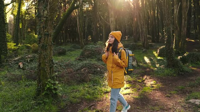 Captivating image of a young woman in a yellow jacket hiking alone, soaking in the serene beauty of a green forest bathed in sunlight.