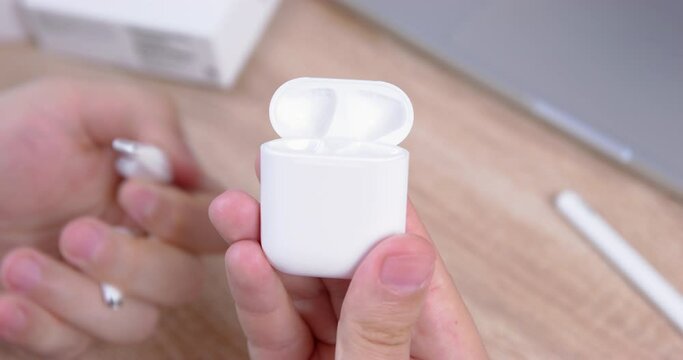 Hand opens charging case and pulls out wireless headphones, puts it on table
