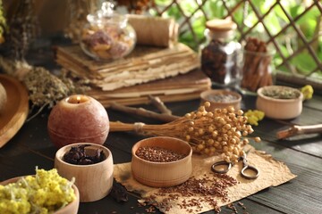 Different dry herbs, flowers, burning candle and scissors on black wooden table indoors
