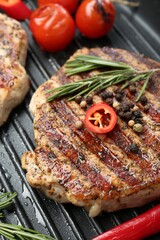 Delicious pork steak, spices and vegetables on grill pan, closeup