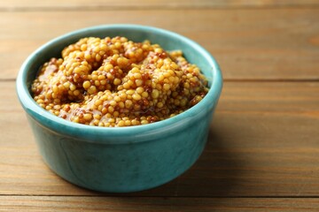 Fresh whole grain mustard in bowl on wooden table, closeup. Space for text