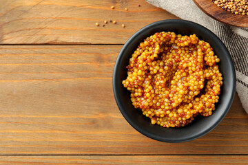 Fresh whole grain mustard in bowl on wooden table, top view. Space for text