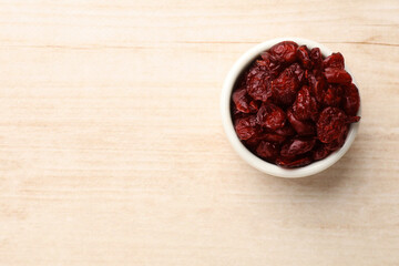 Dried cranberries in bowl on wooden table, top view