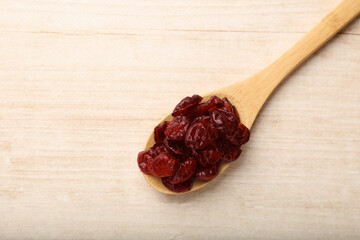 Spoon with dried cranberries on wooden table, top view. Space for text
