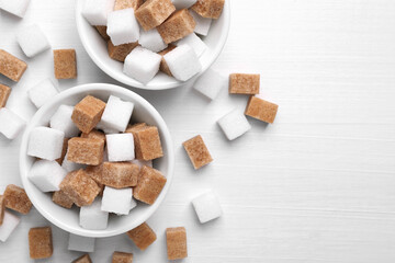 Different sugar cubes in bowls on white wooden table, flat lay. Space for text